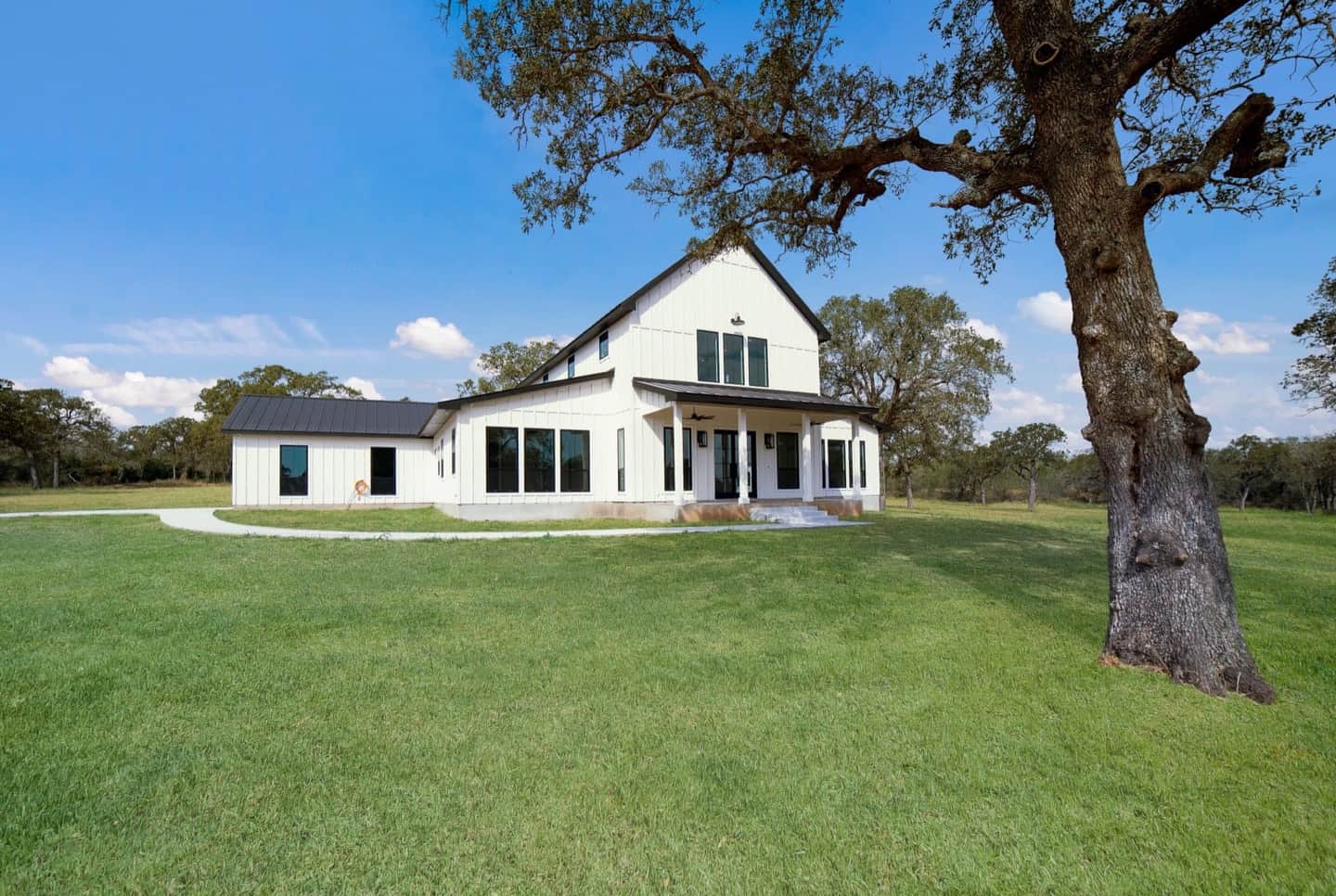 A finished white TKG farmhouse under an old oak tree